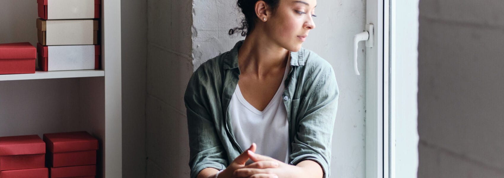 Young beautiful pensive woman with dark curly hair sitting on wi